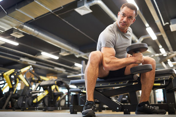 Fototapeta na wymiar Low angle portrait of mature muscular man doing exercises with dumbbells during strength workout in modern gym, copy space
