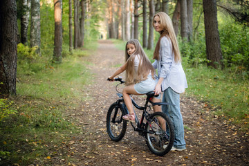 Fototapeta na wymiar Mother taking his child for bycicle ride. Help with a first ride on a bike.