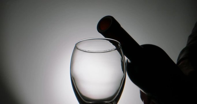 Closeup shot of glass being filled up with stream of alchoholic red wine in slow motion, pouring beverage into goblet, isolated on white background