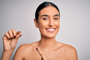 Young beautiful brunette woman holding dental aligner orthodontic to teeth corretion very happy pointing with hand and finger