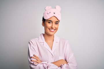 Young beautiful brunette woman wearing pajama and sleep mask over white background happy face smiling with crossed arms looking at the camera. Positive person.