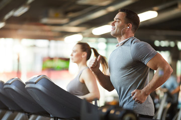 Waist up portrait of mature muscular man running on treadmill while enjoying cardio workout with music in modern gym, copy space