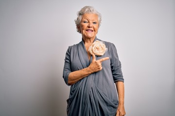 Senior beautiful grey-haired woman wearing casual dress standing over white background cheerful with a smile on face pointing with hand and finger up to the side with happy and natural expression