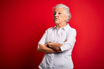 Senior beautiful woman wearing elegant shirt standing over isolated red background looking to the side with arms crossed convinced and confident