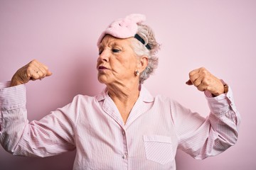 Senior beautiful woman wearing sleep mask and pajama over isolated pink background showing arms...