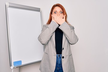 Young beautiful redhead businesswoman doing business presentation using magnetic board shocked...