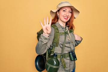 Young redhead backpacker woman hiking wearing backpack and hat over yellow background showing and...