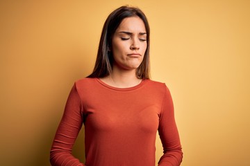 Fototapeta premium Young beautiful brunette woman wearing casual t-shirt standing over yellow background with hand on stomach because indigestion, painful illness feeling unwell. Ache concept.