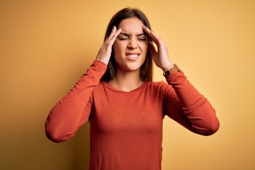 Young beautiful brunette woman wearing casual t-shirt standing over yellow background with hand on headache because stress. Suffering migraine.