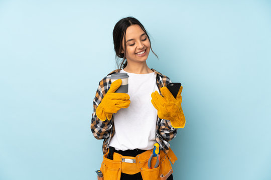 Young electrician woman isolated on blue background holding coffee to take away and a mobile