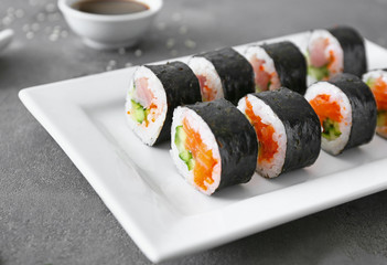 Plate with tasty sushi rolls on table