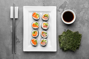 Plate with tasty sushi rolls and soy sauce on grunge background
