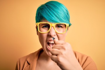 Fototapeta na wymiar Young beautiful woman with blue fashion hair wearing casual glasses over yellow background annoyed and frustrated shouting with anger, crazy and yelling with raised hand, anger concept