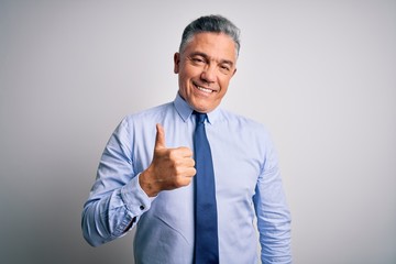 Middle age handsome grey-haired business man wearing elegant shirt and tie doing happy thumbs up gesture with hand. Approving expression looking at the camera showing success.
