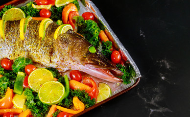 Fresh pike with vegetables and spices on baking tray.