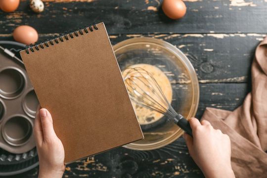 Woman With Cook Book Making Dough At Table, Top View