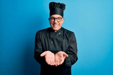 Middle age handsome grey-haired chef man wearing cooker uniform and hat Smiling with hands palms together receiving or giving gesture. Hold and protection