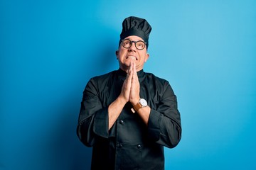 Middle age handsome grey-haired chef man wearing cooker uniform and hat begging and praying with hands together with hope expression on face very emotional and worried. Begging.