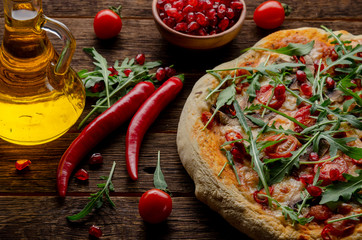 Vegan pizza with fresh garnet and arugula leaves on old wooden background