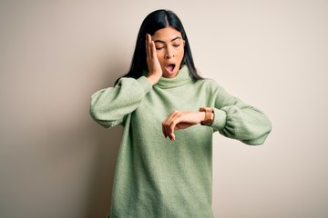 Young beautiful hispanic woman wearing green winter sweater over isolated background Looking at the watch time worried, afraid of getting late