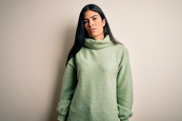 Young beautiful hispanic woman wearing green winter sweater over isolated background Relaxed with serious expression on face. Simple and natural looking at the camera.