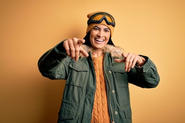 Young beautiful hispanic woman wearing ski glasses and coat for winter weather pointing to you and the camera with fingers, smiling positive and cheerful