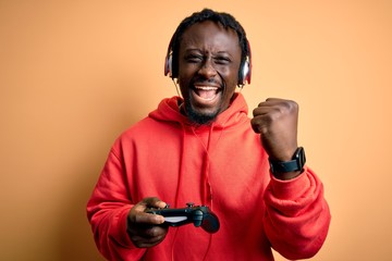 Young african american gamer man playing video game using joystick and headphones screaming proud and celebrating victory and success very excited, cheering emotion © Krakenimages.com