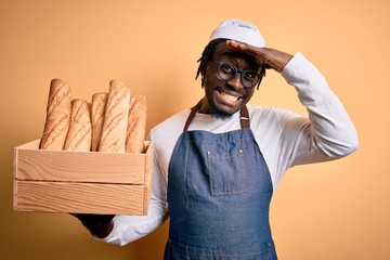 Young african american baker man wearing apron holding wooden box with homemade bread stressed with...