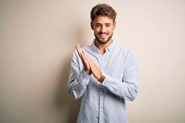Young handsome man with beard wearing striped shirt standing over white background clapping and...
