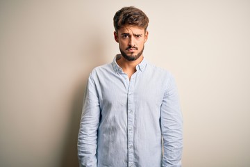 Young handsome man with beard wearing striped shirt standing over white background skeptic and nervous, frowning upset because of problem. Negative person.