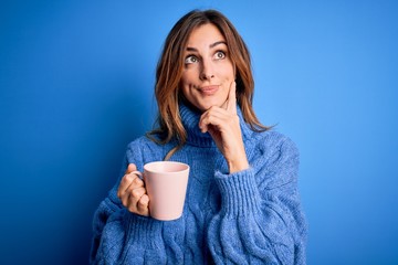 Young beautiful brunette woman drinking cup of coffe over isolated blue background serious face thinking about question, very confused idea