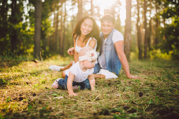 Fototapeta premium little girl one year on the background of parents resting lying on grass learning to walk on nature in the park. The first steps of a child in nature outside the city in the forest