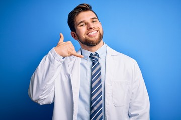 Young blond therapist man with beard and blue eyes wearing coat and tie over background smiling doing phone gesture with hand and fingers like talking on the telephone. Communicating concepts.
