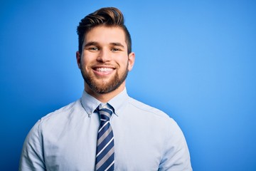 Young blond businessman with beard and blue eyes wearing elegant shirt and tie standing with a happy and cool smile on face. Lucky person.