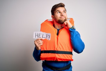 Young blond man with beard and blue eyes wearing lifejacket holding paper with help message serious...