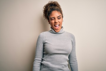 Beautiful african american girl wearing turtleneck sweater standing over white background winking...