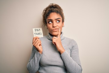 Young african american afro girl holding reminder paper with pay taxes message serious face...