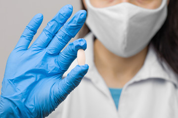 Fototapeta premium A pill in hand in blue gloves. Female is holding a medicine. Drugs against coronavirus,2019-nCoV, SARS-nCov, COVID-2019 outbreaking.