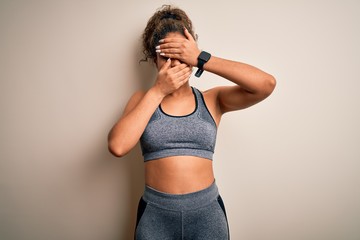 Young african american sportswoman doing sport wearing sportswear over white background Covering eyes and mouth with hands, surprised and shocked. Hiding emotion