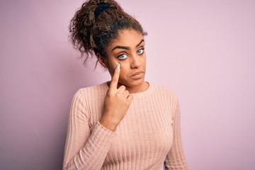 Fototapeta na wymiar Young beautiful african american girl wearing casual sweater standing over pink background Pointing to the eye watching you gesture, suspicious expression