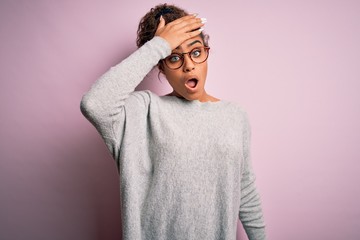 Young beautiful african american girl wearing sweater and glasses over pink background surprised with hand on head for mistake, remember error. Forgot, bad memory concept.