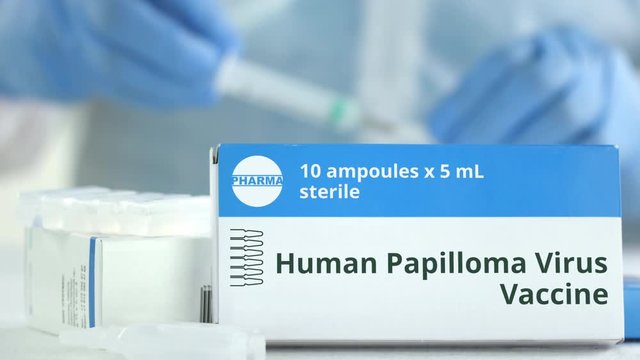 Box with human papilloma virus HPV vaccine on the table against blurred lab assistant or doctor. Fictional phaceutical logo