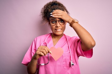 African american cardiologist girl wearing medical uniform and stethoscope holding heart stressed...