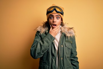 Young african american afro skier girl wearing snow sportswear and ski goggles Looking fascinated with disbelief, surprise and amazed expression with hands on chin