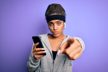 Fototapeta na wymiar African american sporty woman doing sport listening to music using smartphone and earphones pointing with finger to the camera and to you, hand sign, positive and confident gesture from the front