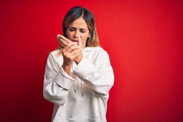 Middle age beautiful sportswoman wearing casual sweatshirt over isolated red background Suffering pain on hands and fingers, arthritis inflammation