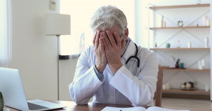 Worried upset senior old adult male doctor feels depressed regrets medical malpractice sitting alone in office. Desperate sad elder surgeon thinking of grief, suffering from burnout or guilt concept.
