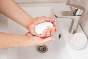 A man holds soap in his hands over the washbasin.