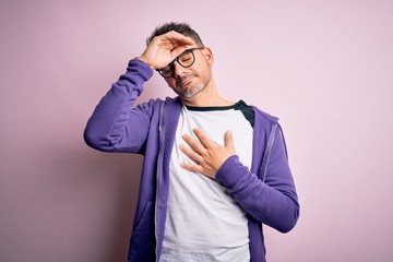 Young handsome man wearing purple sweatshirt and glasses standing over pink background Touching forehead for illness and fever, flu and cold, virus sick