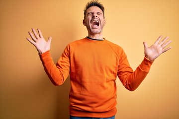 Young handsome man wearing orange casual sweater standing over isolated yellow background...